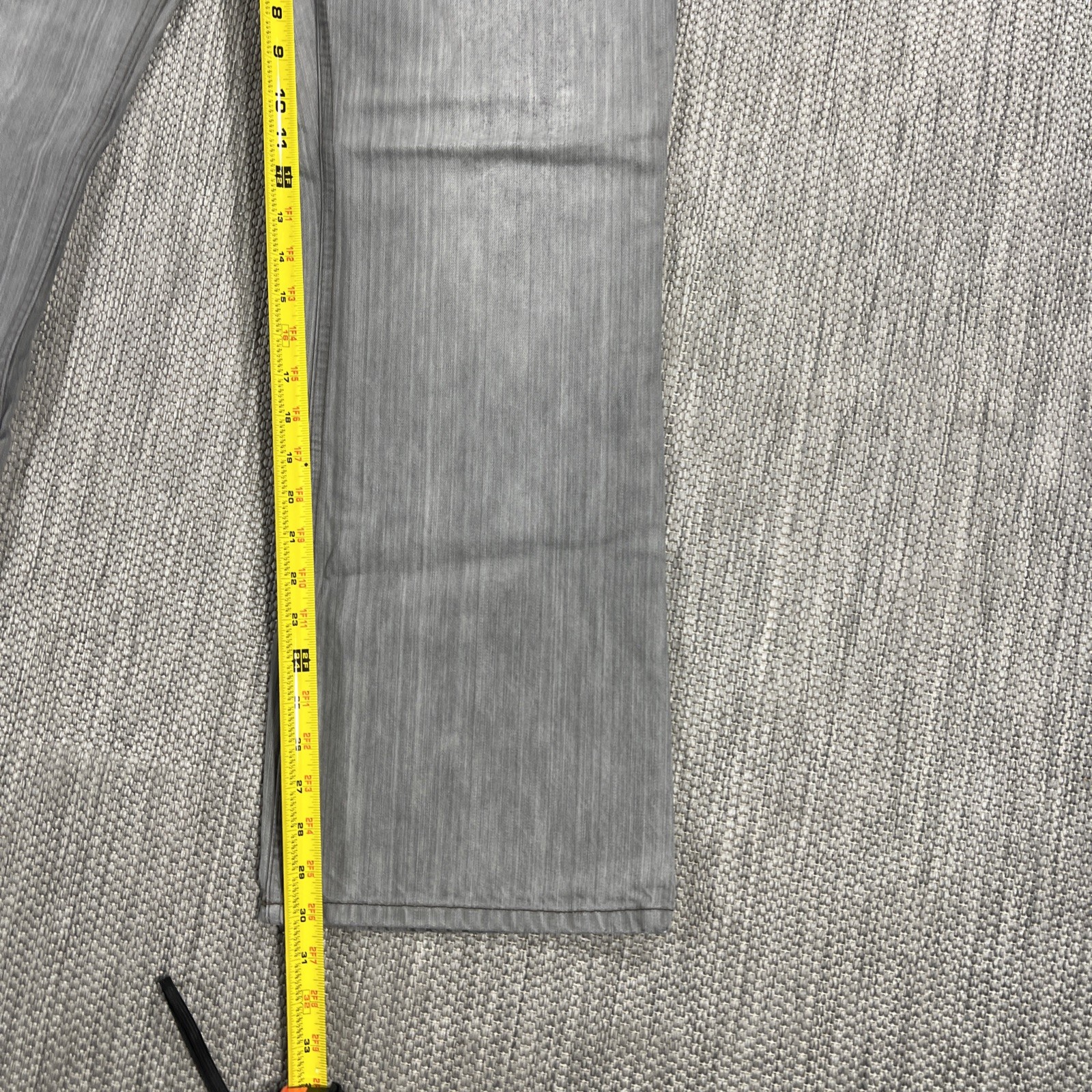 Gray Armani Exchange men’s 34X30 denim with yellow measuring tape along the length of the left leg.