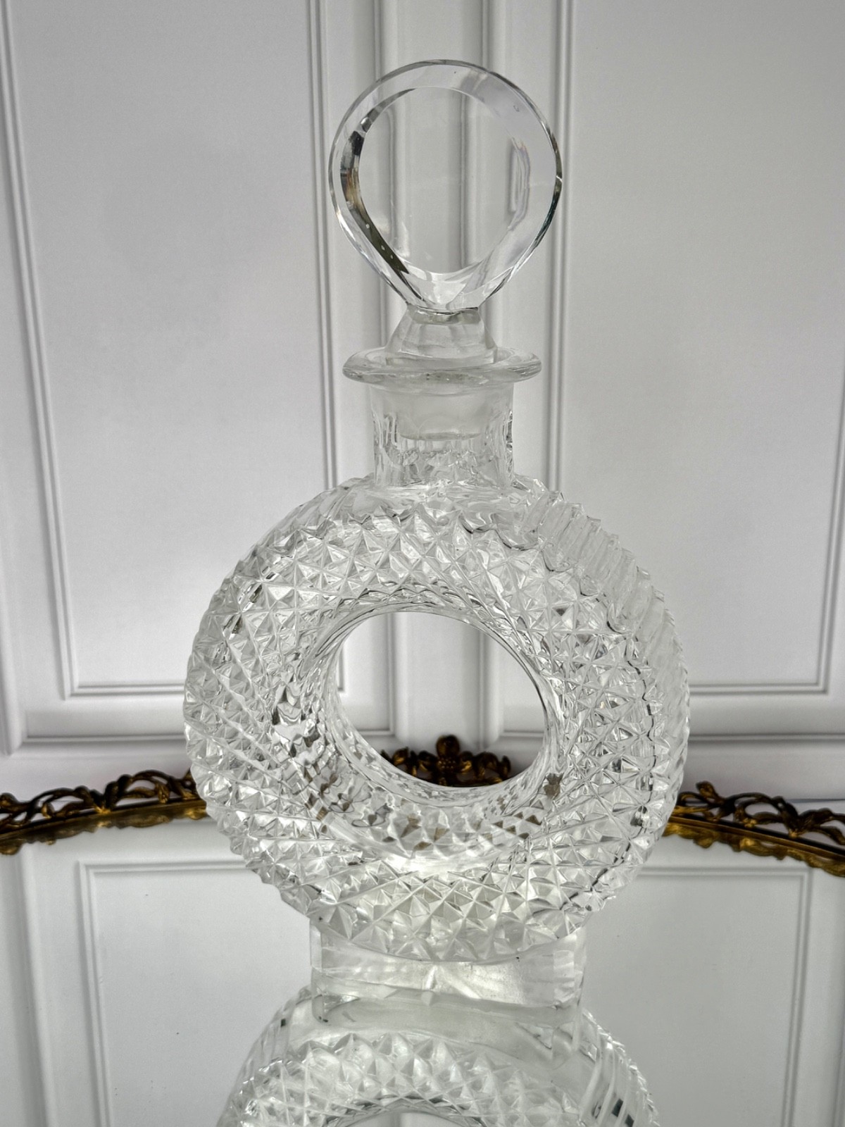 Clear cut-crystal decanter with a donut-ring body and a geometric stopper.