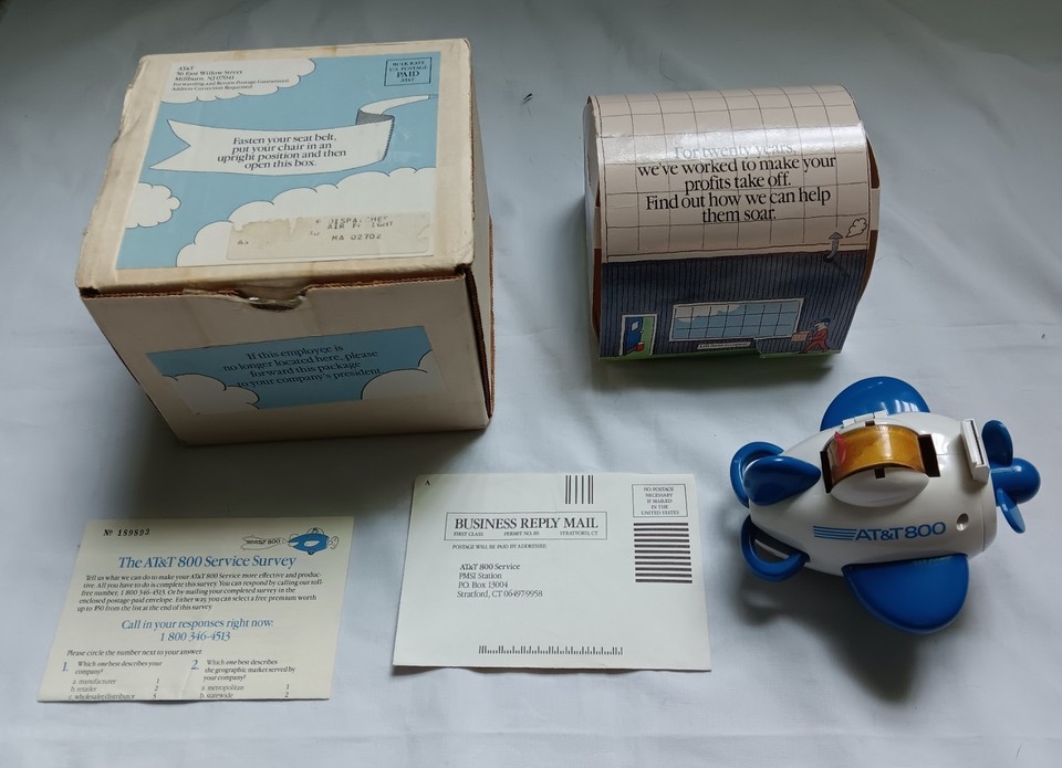 A vintage AT&T corporate gift combo — tape dispenser and stapler shaped like an airplane — peak mid-century corporate kitsch.