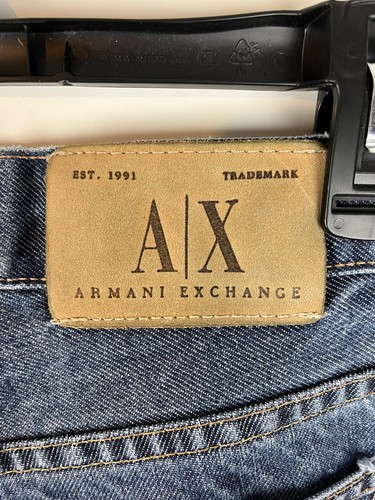 Brown leather AX Armani Exchange J40 patch with black clasp, yellow stitching, and white “AX” logo on denim fabric.