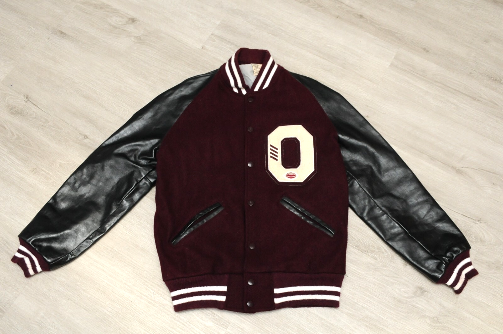 Maroon varsity jacket with black leather sleeves, white buttons, and large white “O” logo on front, size 38.