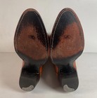 Brown leather cowboy boots with black insoles, dark heel panel, and subtle orange laces on a white background.