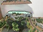 Z scale model railway layout with rocky cliffs, tunnel, river, trees, and painted water features.