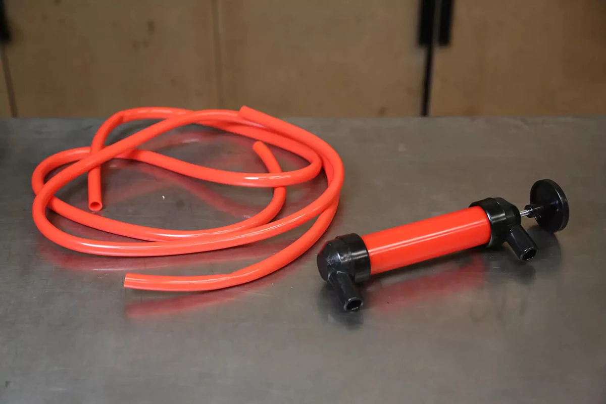 An orange transfer pump with orange tubing sits on a work surface.