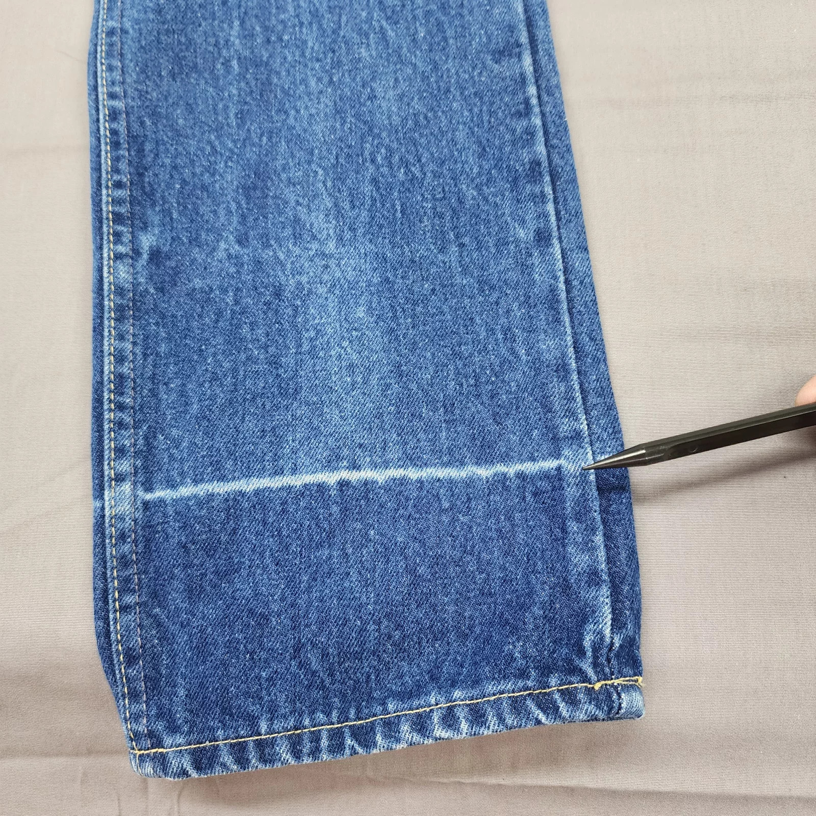 Blue denim high-rise straight leg with yellow stitching, marked by a black vertical line and white fabric fold.