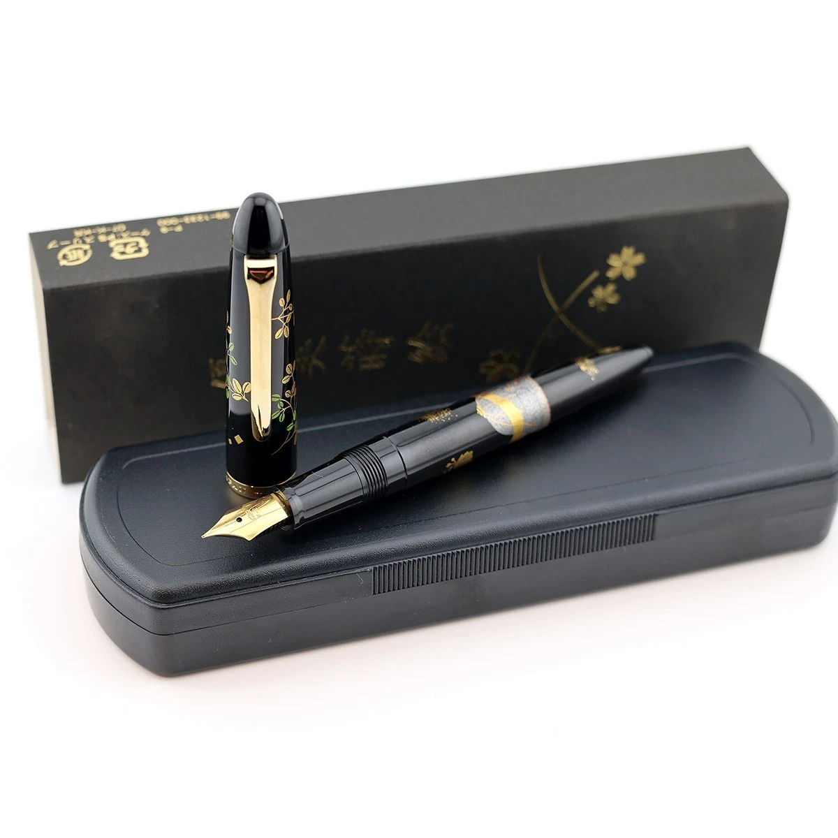 Black Sailor Maki-e fountain pen with gold accents and green leaves, displayed in a black box with labeled lid.
