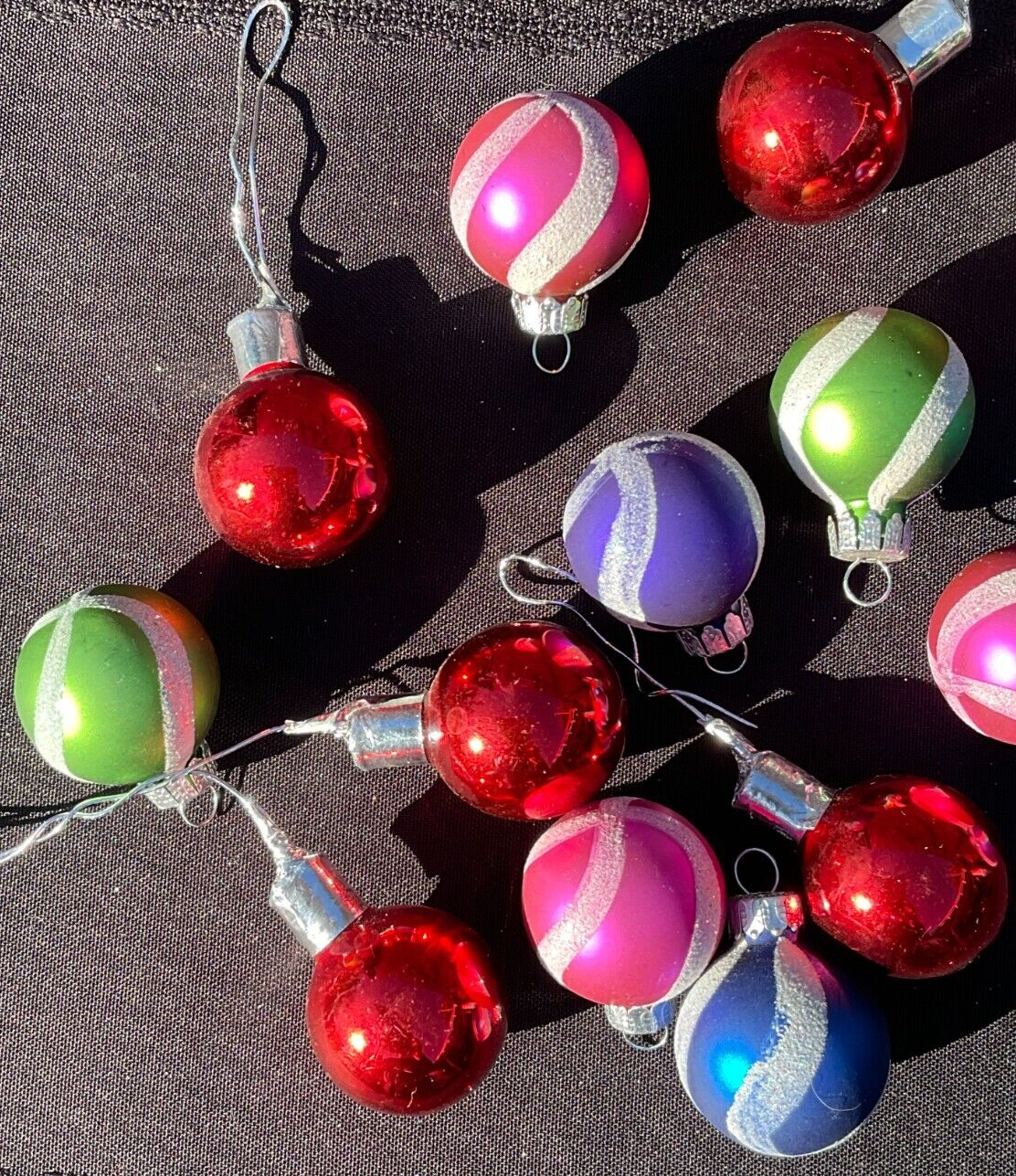 String of 16 round Christmas balls with multicolor horizontal stripes in red, silver, and green, hanging on black fabric.