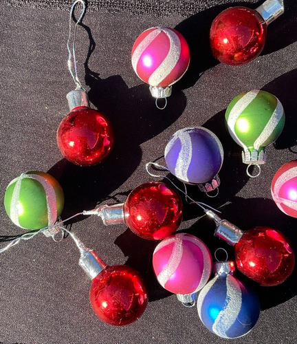String of 16 round Christmas balls with multicolor horizontal stripes in red, silver, and green, hanging on black fabric.