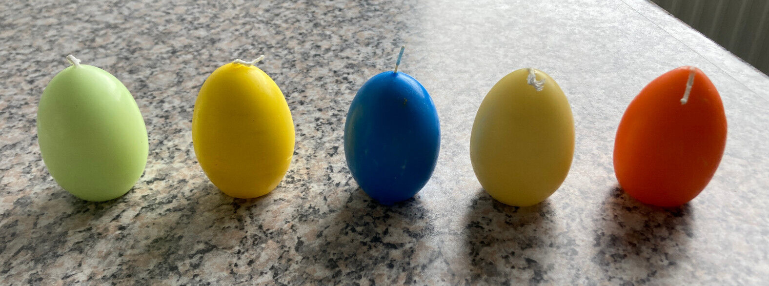 5 Kerzen in Eiform: blau, orange, hellgrün und 2 Gelbtöne