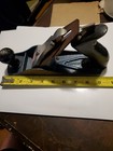 Vintage blackhawk C557MP wood hand plane with flat bottom, silver blade, and yellow tape measure on white surface.