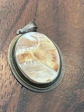This is an antique carved shell cameo pendant or brooch with a sterling silver