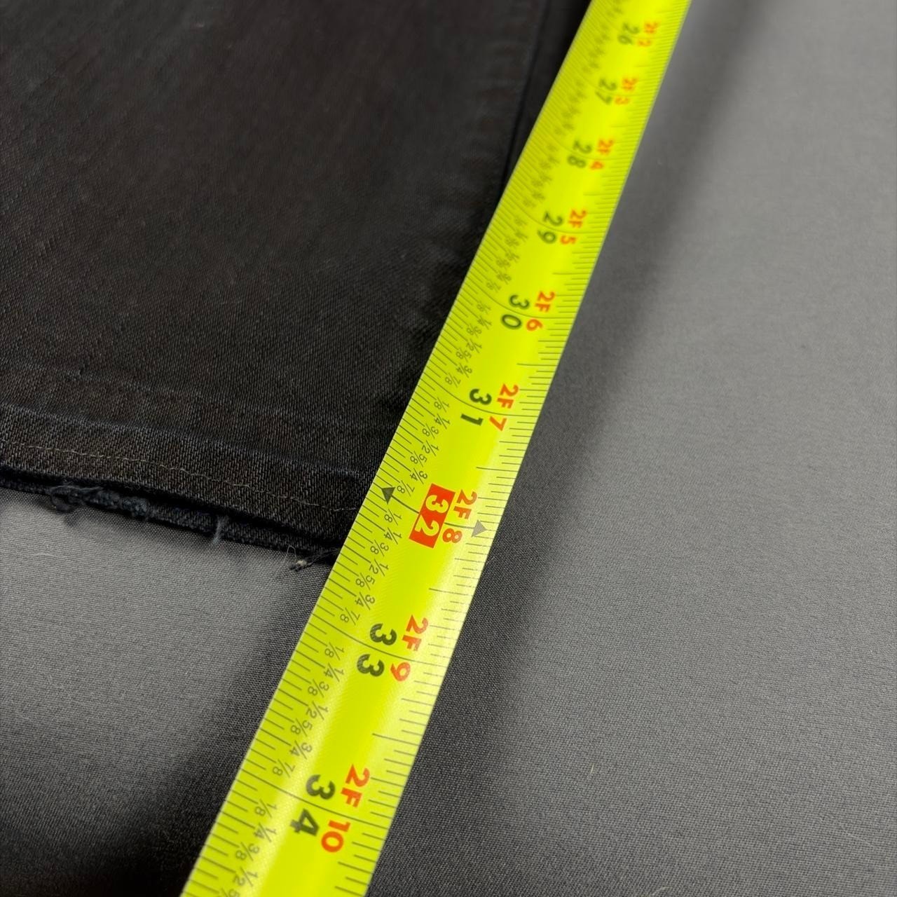 Black faded bootcut jeans with visible yellow measuring tape along the waistband, showing size 33 and 36.
