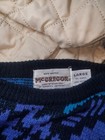 White fabric tag on black sweater with blue acrylic, size large, made in USA, care rev label visible.