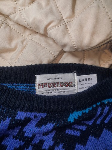White fabric tag on black sweater with blue acrylic, size large, made in USA, care rev label visible.