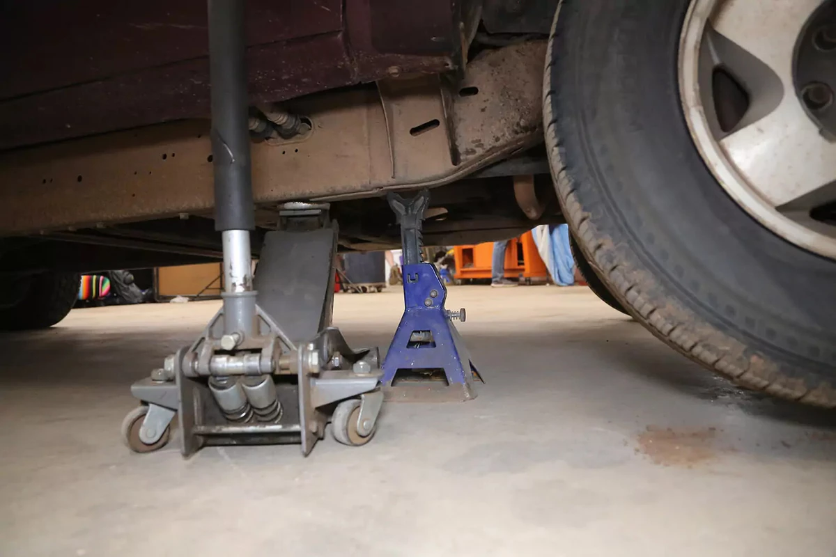 A floor jack and jack stand underneath a car.