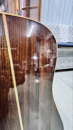 Brown acoustic guitar with gold hardware, subtle scratches, and glossy finish on a light wood fretboard.