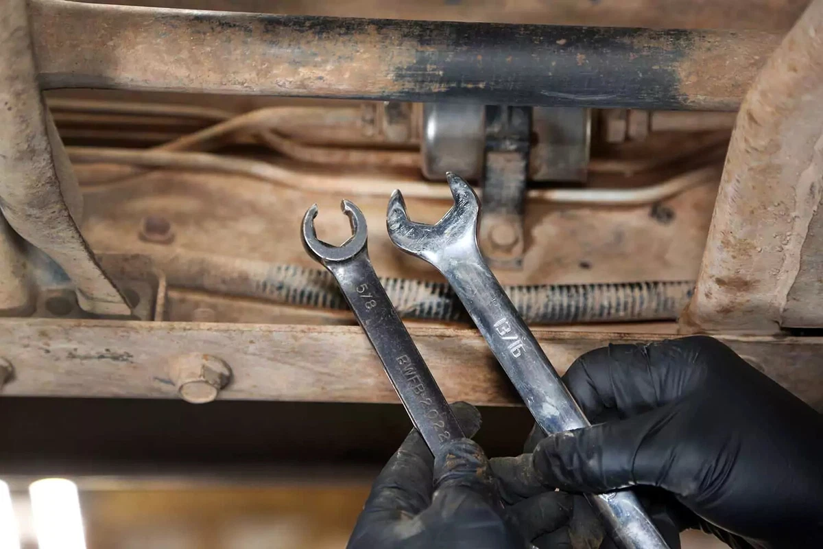 A mechanic holding a line wrench and an open-end wrench.