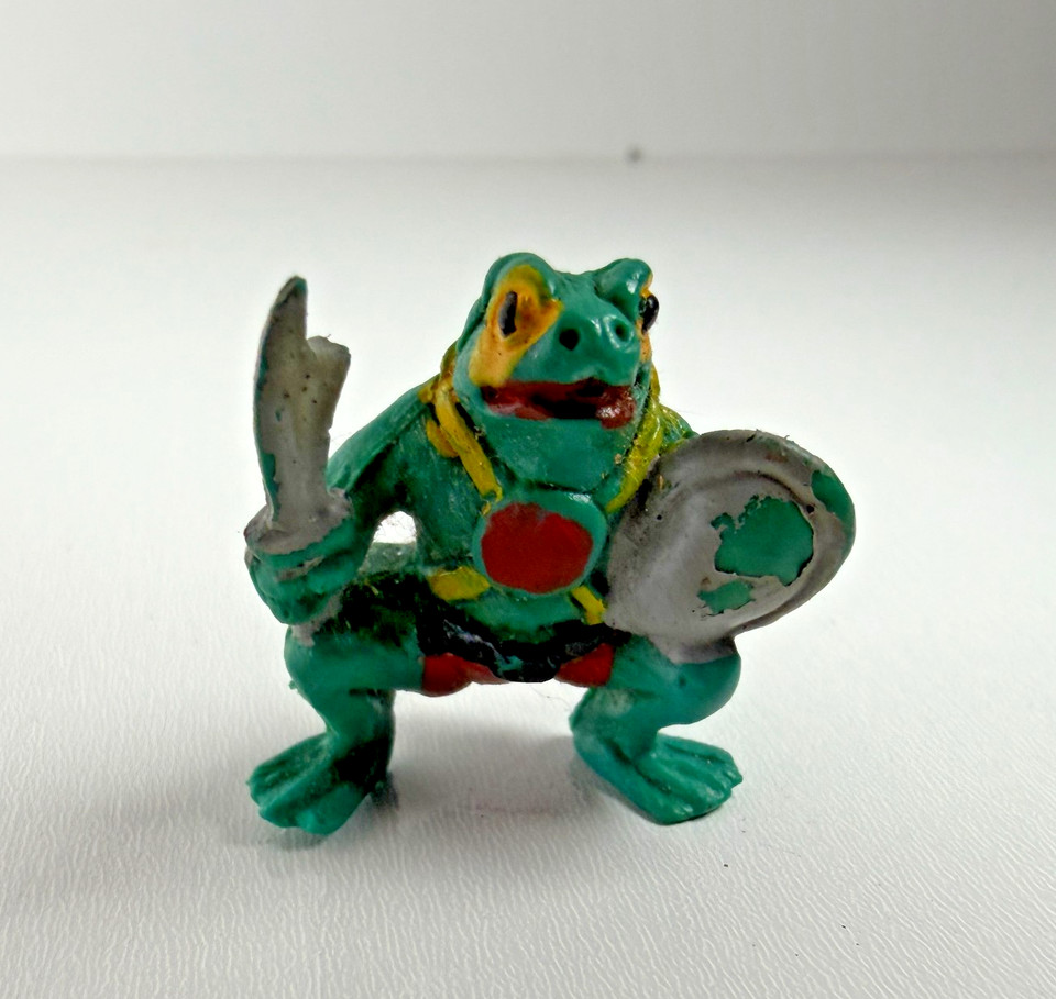 A rare vending machine-era frog warrior clutching a sword and shield — the kind of absurd, charismatic mini that stops people mid-conversation.