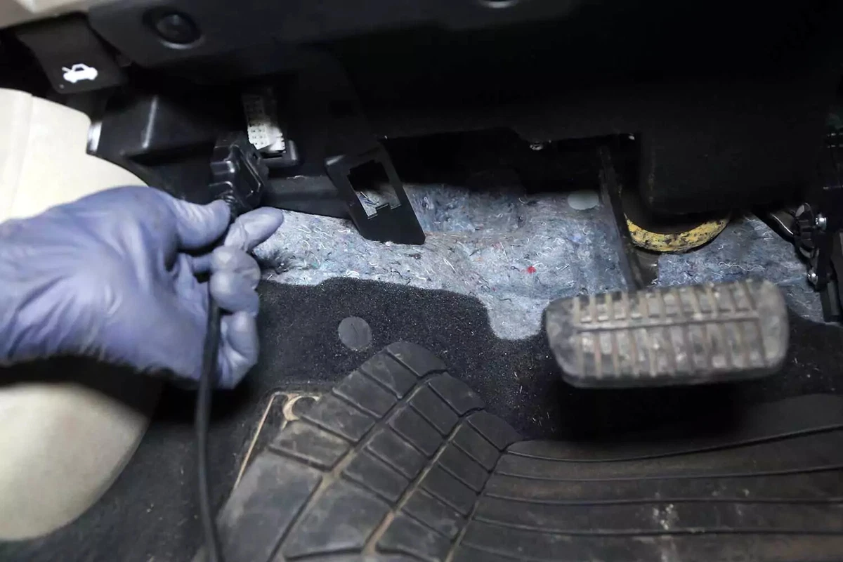 A hand connects a code reader to an OBDII port.