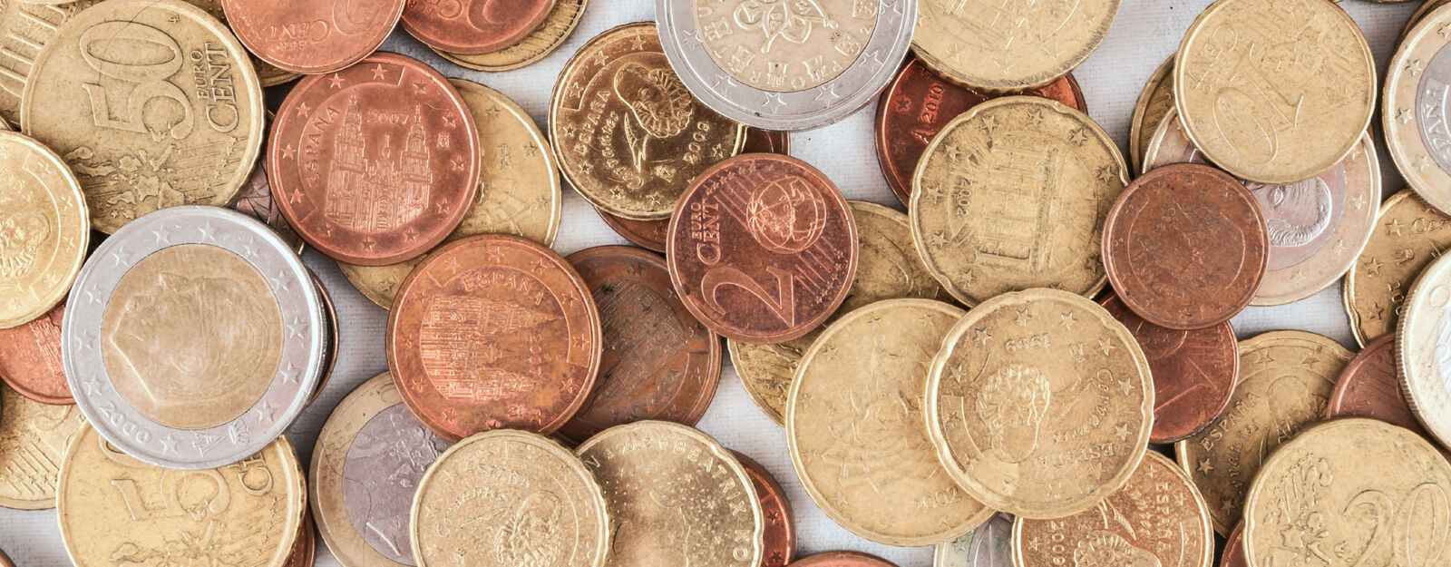 Nahaufnahme von unterschiedlichen Euro-Münzen, die willkürlich aufeinander platziert auf einer hellen Unterlage liegen.