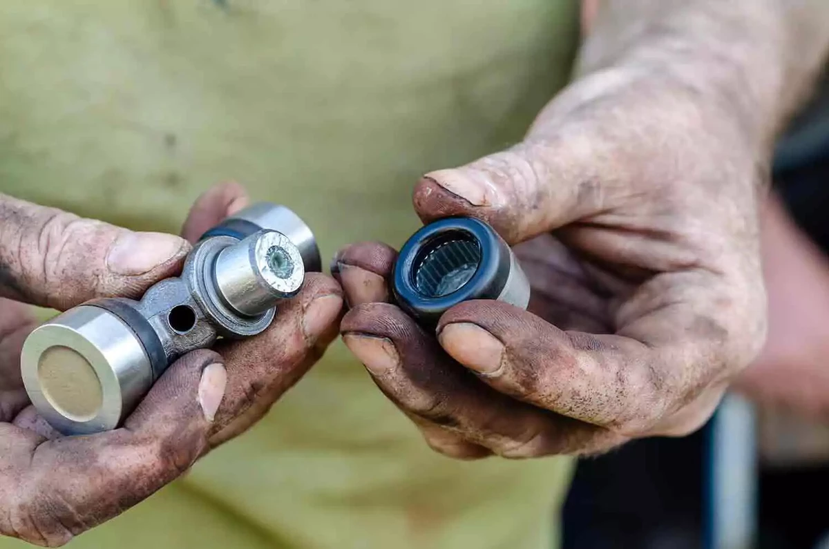 A close-up view of a mechanic holding a brand new u-joint in his right hand and a bearing in his left hand.