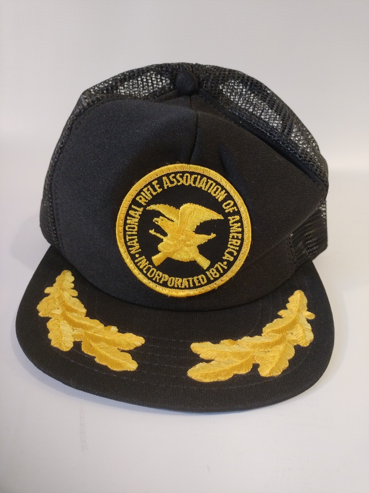 Black trucker hat with yellow National Rifle Association logo and text, featuring two yellow leaf emblems on the front panel.