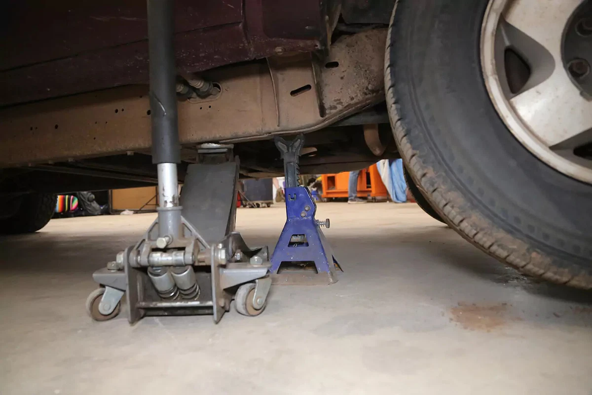 A floor jack and jack stand support a vehicle.