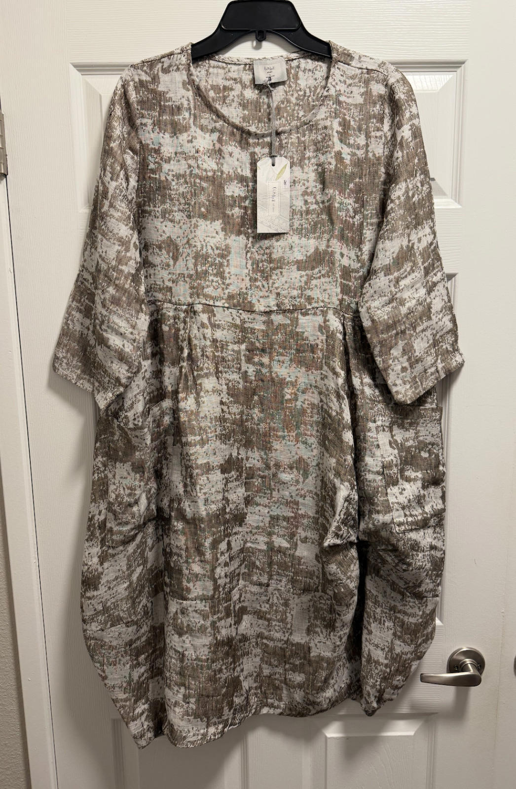 Gray linen long sleeve dress with subtle textured pattern, round neckline, and front pockets, hanging on black hanger.