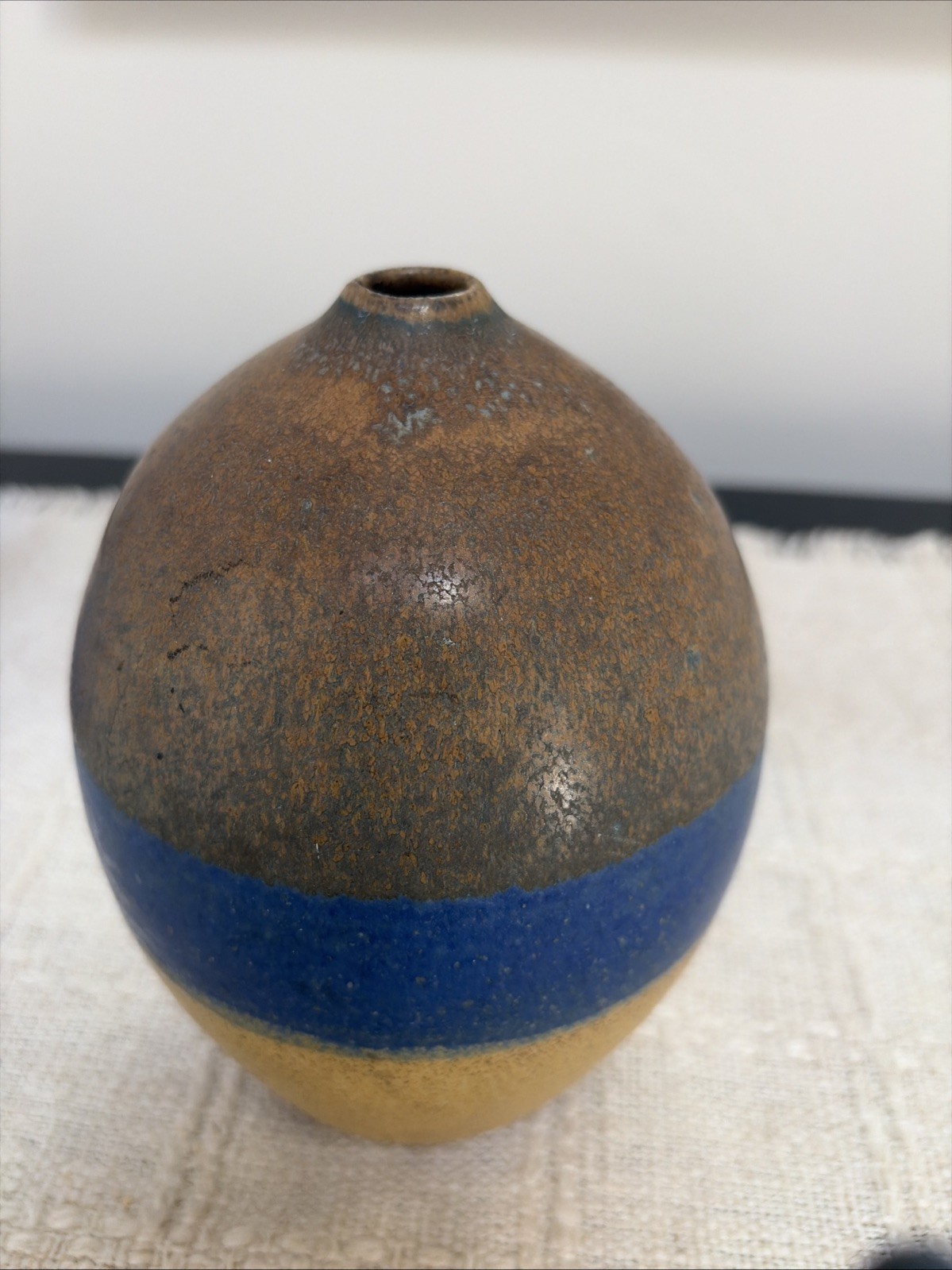 Small mid-century studio pottery weed pot vase glazed in blue, brown, and tan.