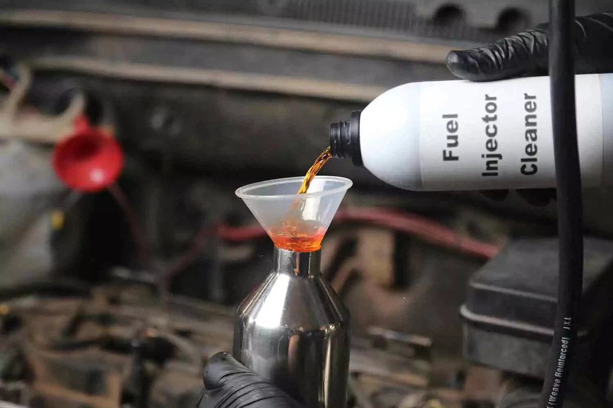 A mechanic pours fuel injector cleaner from a white bottle into the cleaning kit canister.