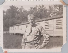 WW2 Photo of Soldier Smiling Beside Long Wooden Barracks Row