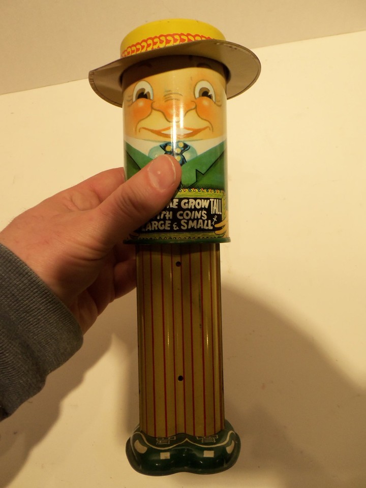 A charming mid-century tin litho mechanical bank that actually grows taller as you stack coins — pure Americana novelty engineering from a bygone era.