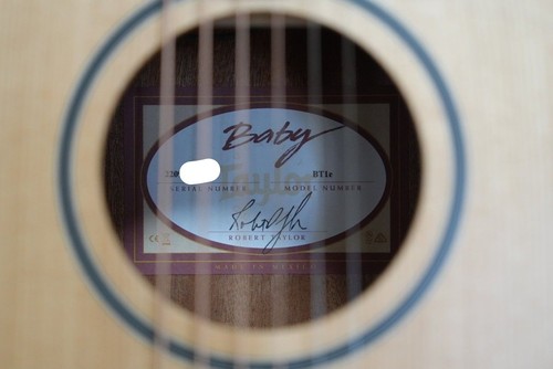 Baby Taylor BT1e electric acoustic guitar with light wood fretboard, silver hardware, and blue autograph label on inner wall.