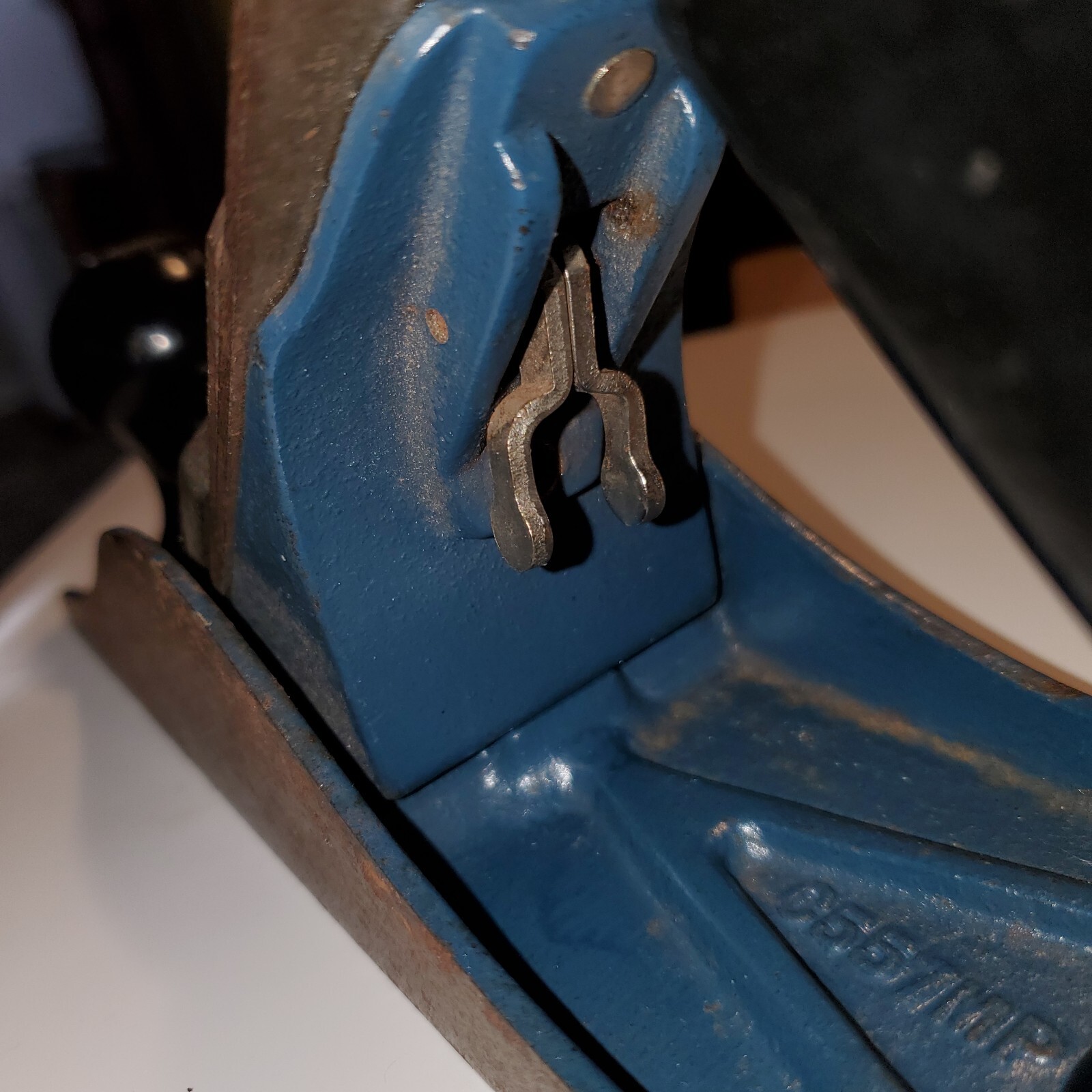 Close-up of worn blue metal hand plane with flat rectangular base and silver corner bracket, engraved “C557MP Made in USA.”