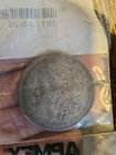 1890 $1 VG-VF Morgan Silver Dollar in clear, unopened APMEX bag