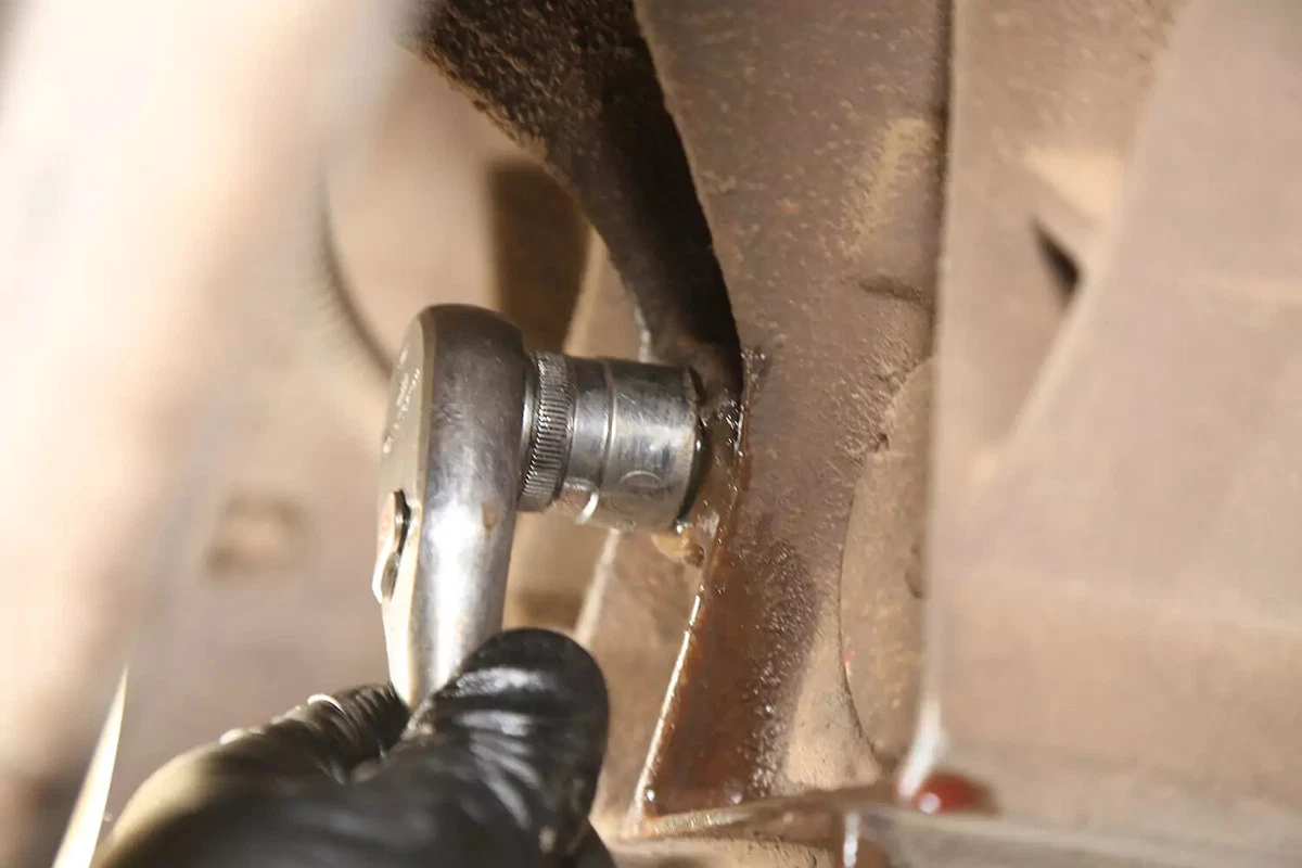 A mechanic wearing a black glove uses a torque wrench to tighten the transfer case's fill plug.