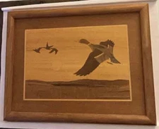 A framed wooden inlay artwork depicting ducks in flight.