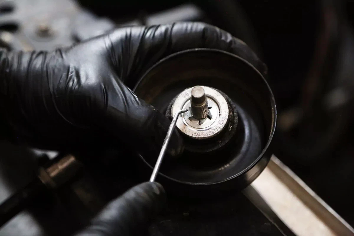 A mechanic uses a pick to lift the keeper ring away from the idler pulley.