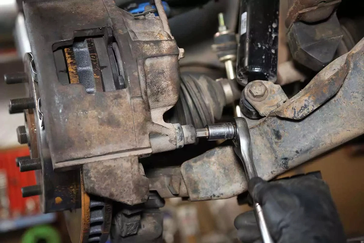 A mechanic removes a brake caliper bolt with a socket wrench.