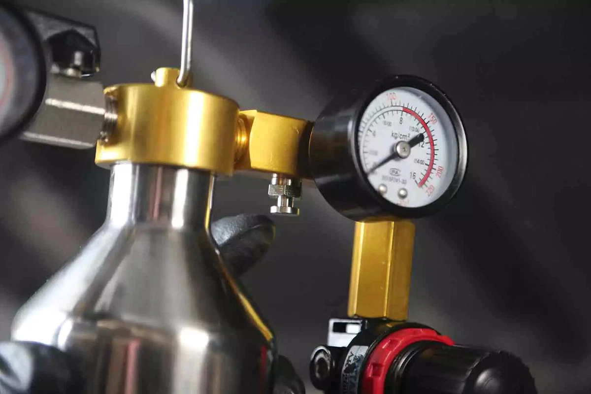 A mechanic wearing a black glove pushes the purge valve.