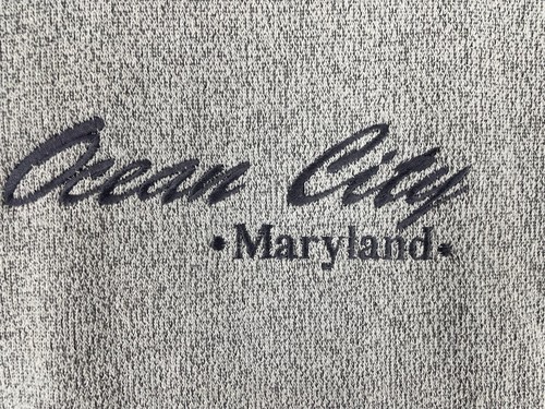 Gray vintage pullover sweater with navy “Ocean City Maryland” text and wavy line accents on chest and shoulders.