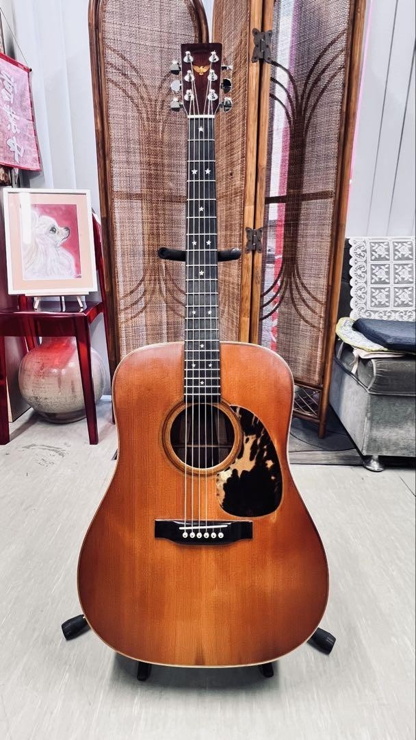 Brown acoustic guitar with f-holes, silver hardware, and visible scratches, S/N 375511, on stand in living room.