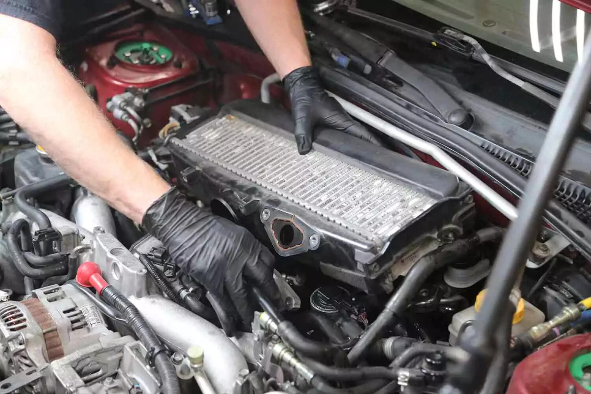 A mechanic wearing black gloves replaces components in an engine.