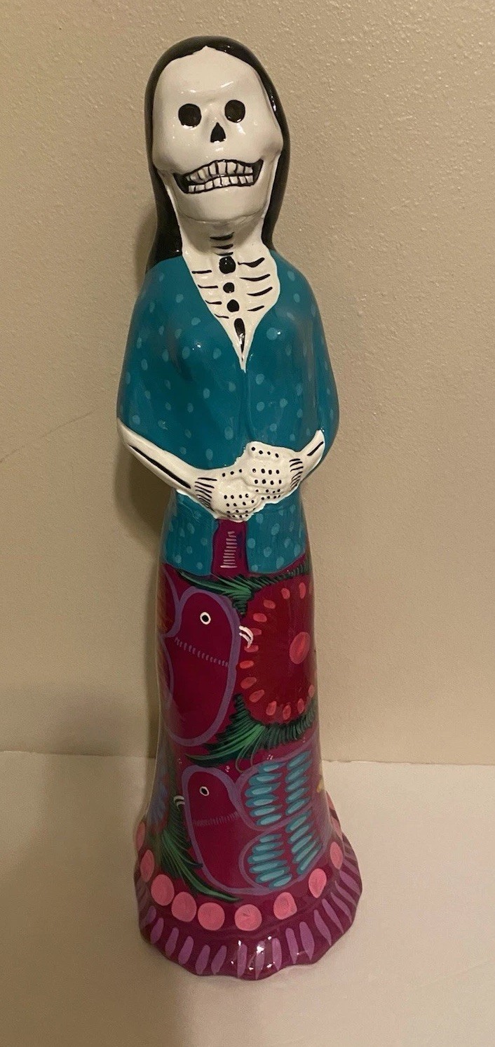 A smaller hand-painted ceramic Catrina figurine in a colorful dress with a decorated skull face.