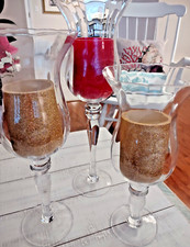 Three Clear Glass Hurricane Style Pedestal Candle Holders of Varying Heights.