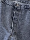 Close-up of worn black Levi’s 501 XX jeans with visible stitching and button fly closure on a textured gray surface.