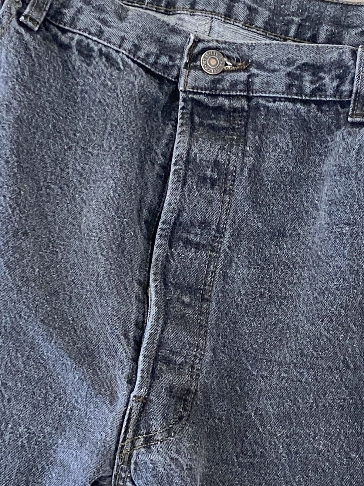 Close-up of worn black Levi’s 501 XX jeans with visible stitching and button fly closure on a textured gray surface.