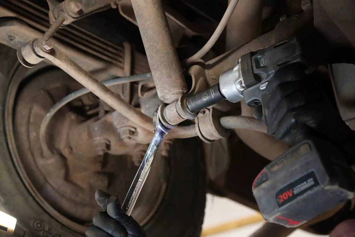 The lower bolt on the rear shock absorber is removed with a wrench and an impact gun.