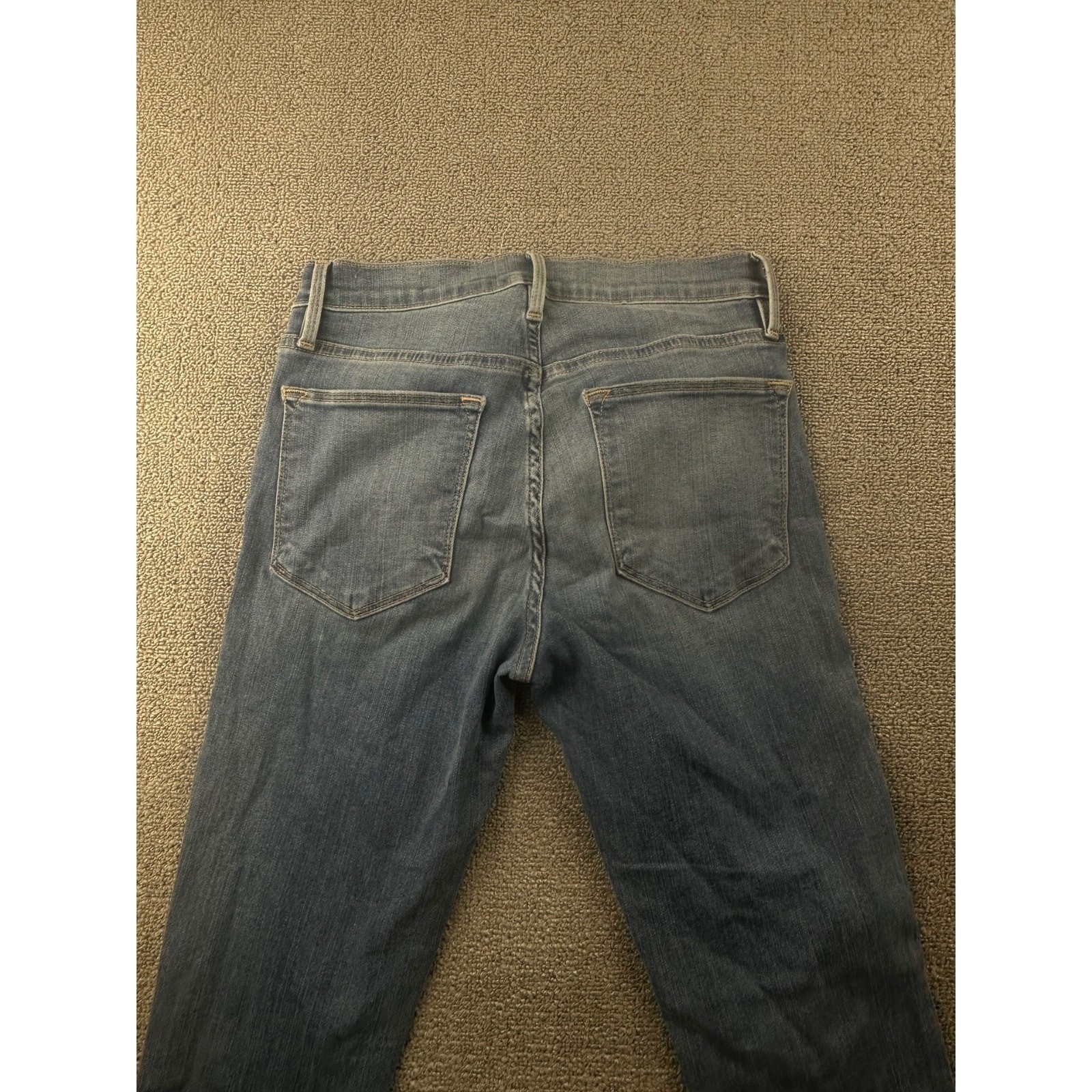 Back view of Frame Jeans women 25 with frayed hems, two pockets, and belt loops on beige fabric surface.