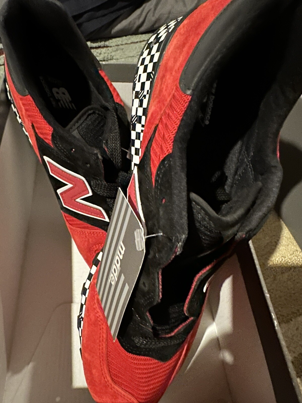 Red and black New Balance 1300AP sneakers with white checkered flag design, suede panels, and gray Made In USA tag.